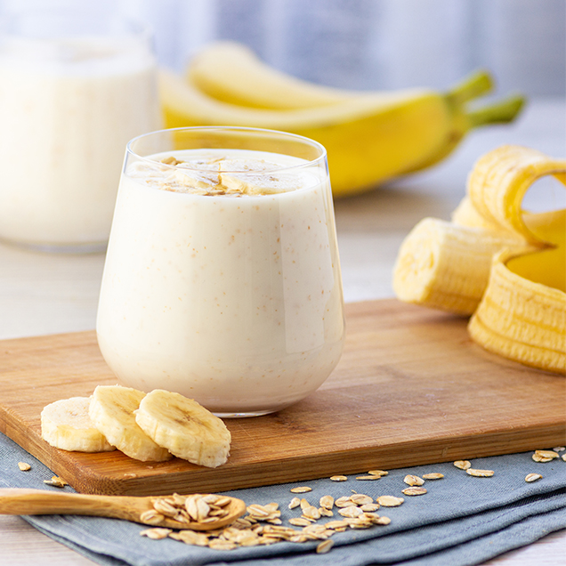 Bananensmoothie auf Holzbrett mit frischen Bananen im Hintergrund.